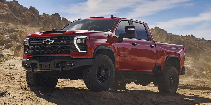 A red Chevrolet Silverado 2500HD pickup truck parked in a rugged, desert landscape.