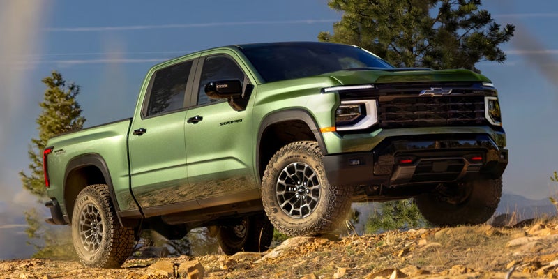2027 Chevrolet Silverado 1500 pickup climbs over rocky off-road terrain.